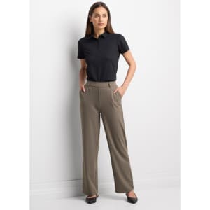 A woman wearing a black short sleeve polo shirt paired with beige trousers, standing confidently with her hands in her pockets.