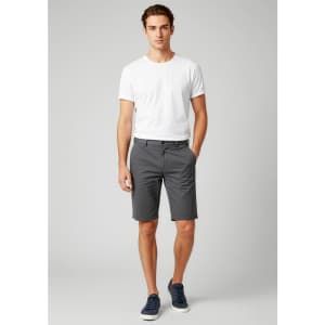 A model wearing grey dress shorts paired with a white t-shirt and navy shoes, featuring a branding logo.