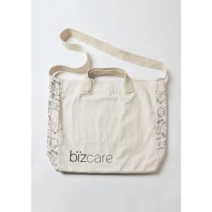 A beige unisex tote bag featuring a patterned edge and a logo. It has two carrying handles and a shoulder strap.