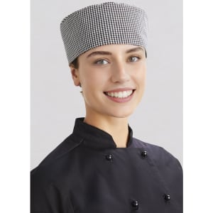 A chef wearing a black uniform and a checked white and black "Chef Cap", smiling at the camera.