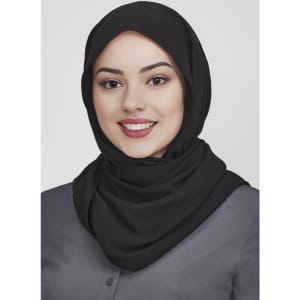 A black women's hijab is worn by a woman with a confident smile, set against a neutral background.