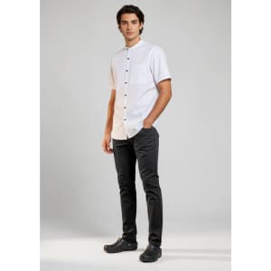 A man stands wearing black chef flex pants paired with a short-sleeve white shirt. The outfit includes a logo.