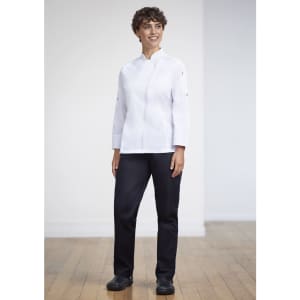 A woman stands wearing a white uniform top and navy scrub bottoms, paired with black shoes, in a bright indoor setting.