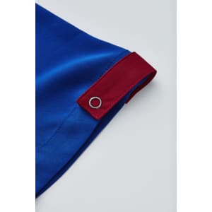 A blue unisex scrub top featuring a red accent and a silver eyelet detail.