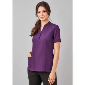 A women's tunic in a rich purple colour with short sleeves and pockets, featuring a button-up placket and a logo.