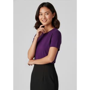 A woman models a purple short sleeve jersey top, paired with a black skirt. The top features a subtle logo.