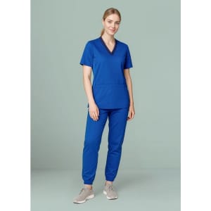 A woman wearing blue women's Riley slim leg jogger scrub pants paired with a matching scrub top, standing against a light background.