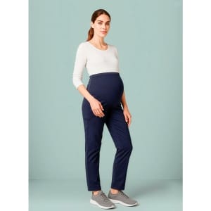 A pregnant model wearing navy maternity scrub pants paired with a light-coloured top and grey shoes.