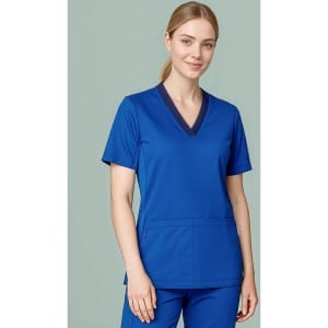 A women's blue scrub top featuring a V-neck design and a front pocket, worn by a model.
