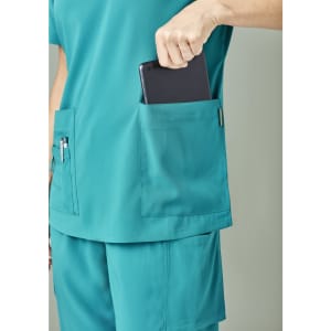 A teal scrub top featuring two pockets, with a hand placing a tablet into one of them.