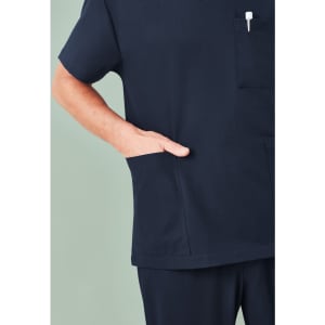 A navy unisex V-neck scrub top featuring short sleeves and a chest pocket. The hand is casually placed in a side pocket.