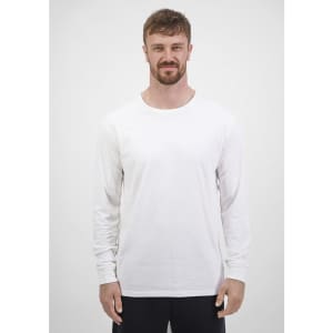 A man wearing a plain white long sleeve tee stands against a neutral background. The tee has a brand logo.