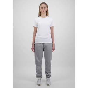 A woman wears a plain white t-shirt and grey track pants, standing against a light grey background. The pants have a logo.