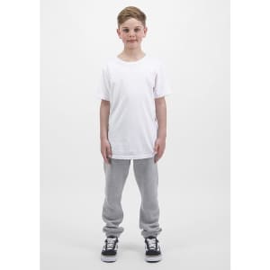 A child stands upright, wearing a plain white t-shirt and grey track pants, with black and white sneakers.