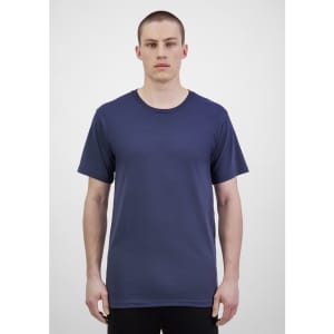 A man wearing a navy blue short sleeve tee, standing against a light grey backdrop. The tee has a logo.