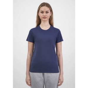 A woman stands wearing a navy short sleeve tee, paired with grey sweatpants, featuring a logo on the tee.