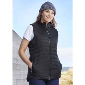 A black women's expedition vest is worn by a woman with a beanie, featuring a zip front and side pockets.