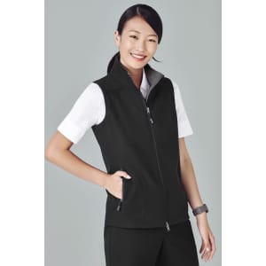 A woman in a black vest smiles while posing, featuring a zippered front and side pockets. The vest has a logo.