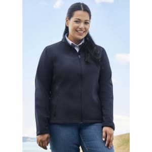 A woman wearing a black soft shell jacket stands outdoors, smiling against a scenic backdrop with blue skies.