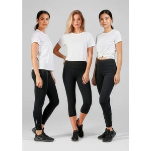 Three women in white t-shirts and black leggings, standing together against a grey background. The leggings have a logo.