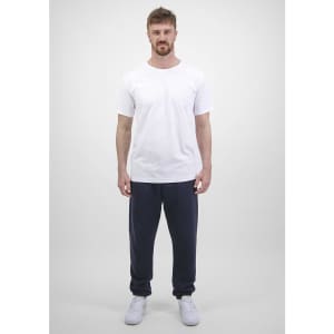 A man stands wearing a white t-shirt and navy blue track pants. The pants have a logo on them.
