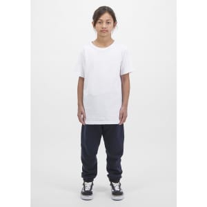 A child wears a white t-shirt and navy track pants, standing against a plain white background. The outfit features a logo.
