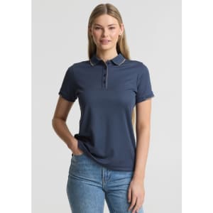 A women's short sleeve polo shirt in navy blue with a collar and a logo. The model is wearing it with jeans.