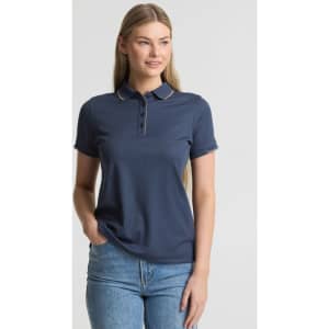 A women's short sleeve polo shirt in navy blue, featuring a collar and a logo. Model stands with one hand in pocket.