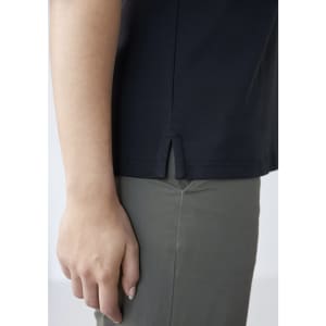 A side view of a navy women's polo shirt featuring a small slit at the hem, paired with light-coloured pants.