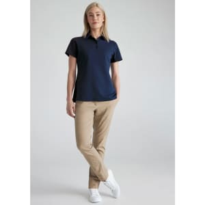 A woman in a navy short sleeve polo shirt paired with khaki trousers and white sneakers. The shirt has a logo.