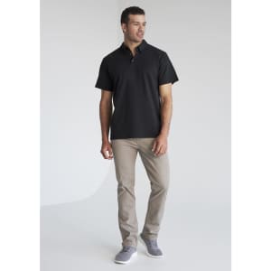 A man wearing a black short sleeve polo shirt and light grey trousers, featuring a logo on the polo.