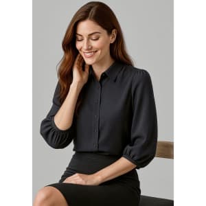 A woman in a black 3/4 sleeve blouse with a button front, sitting on a chair, smiling.