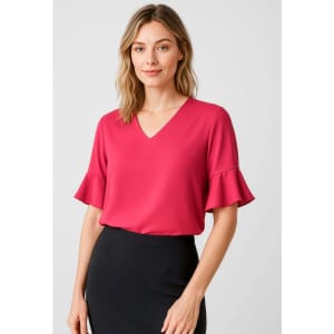 A woman wearing a pink fluted sleeve blouse with a V-neckline, paired with a black skirt. The image features a brand logo.