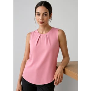 A pink sleeveless blouse with pleat detail, styled with a model standing beside a wooden surface.