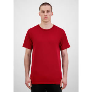 A man stands wearing a red short sleeve t-shirt. The t-shirt has a simple design and features a logo.