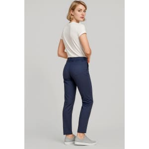 A woman stands wearing navy slim leg stretch chino pants and a white top, paired with grey sneakers.
