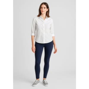A woman stands wearing a white shirt and navy high-rise pull-on leggings, paired with grey shoes. The image includes a logo.