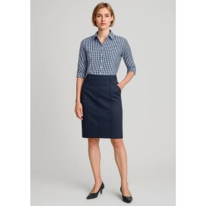 A woman wears a navy mid-waist stretch chino skirt paired with a checked shirt and heels. The outfit includes a logo.