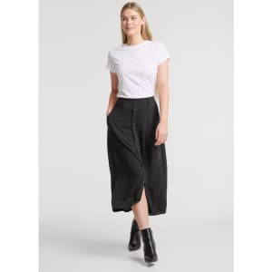 A woman wearing a black maxi skirt paired with a white T-shirt and black ankle boots, featuring a front slit and pockets.