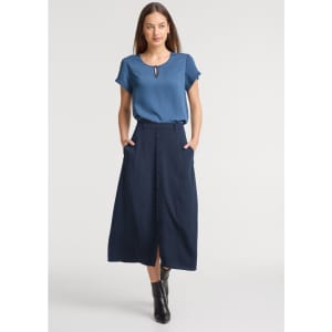 A woman wears a light blue top and a long navy skirt with buttons and pockets. The outfit is stylish and modern.