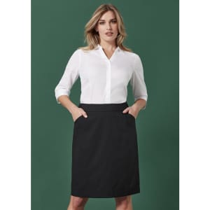 A woman wearing a white button-up shirt and a black functional pencil skirt with pockets, set against a green background.