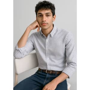 A young man sits in a chair wearing a white button-up shirt with a checked pattern and blue jeans.