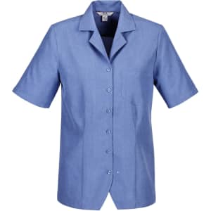 A short-sleeved overblouse in light blue, featuring a collar and a chest pocket, with buttons down the front and a logo.
