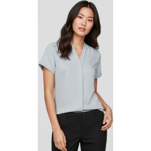 A light blue women's short sleeve button-up shirt displayed on a model, featuring a v-neckline and rolled sleeves.