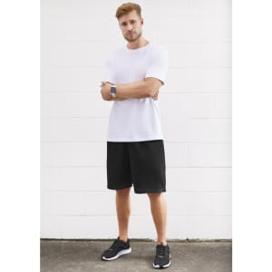A model wearing black sports shorts and a white t-shirt stands against a white wall, with a logo visible on the shorts.