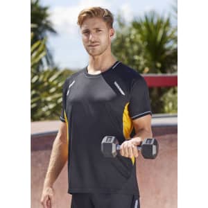 A man holds a dumbbell while wearing a black and yellow short sleeve tee, set against a tropical outdoor background.