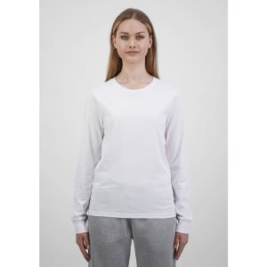 A woman wears a white long sleeve tee, paired with grey trousers. The tee features a simple design and has a logo.