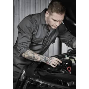 A man wearing a dark grey overall inspects the engine of a car, showcasing detailed tattoos on his arm.