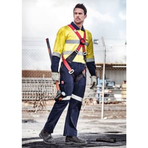 A man wears a yellow and navy rugged cooling overall with safety features. He holds a tool and stands in an industrial setting.