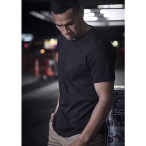 A black men's t-shirt is displayed on a model, set against a blurred urban background with street signs.